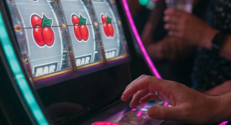 Photo depicting gambling psychology: near-miss slot, hesitant hand, blurred onlookers applying pressure.
